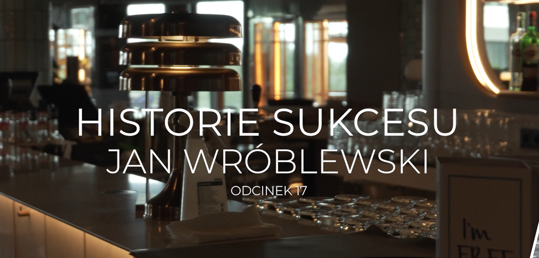 Kadr z baru lub restauracji, na pierwszym planie nowoczesna lampa i blat z kieliszkami. Na środku grafiki duży biały napis: „Historie Sukcesu Jan Wróblewski, Odcinek 17