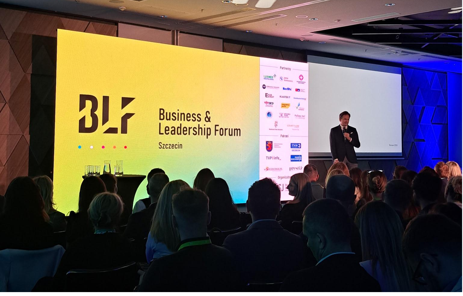 Konferencja Konferencja: prelegent z widownią. Na wyświetlaczu logotyp konferencji Business & Leadership Forum.