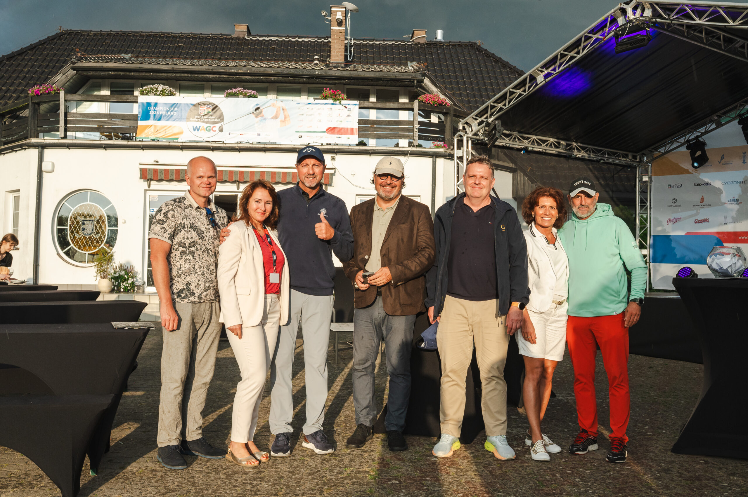 Siedem osób pozuje wspólnie przed sceną podczas wydarzenia golfowego. W tle baner World Amateur Golfers Championship WAGC z napisem Championship 2026 Poland oraz tablica z logotypami partnerów.